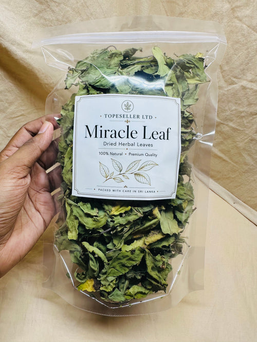 A hand holds a clear plastic bag filled with dried green herbal leaves. The front label reads 'TOPESELLER LTD Miracle Leaf Dried Herbal Leaves' on a beige fabric background.